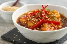 Sauce aigre-douce Suzi Wan brillante avec sésame et poivron rouge dans un bol blanc